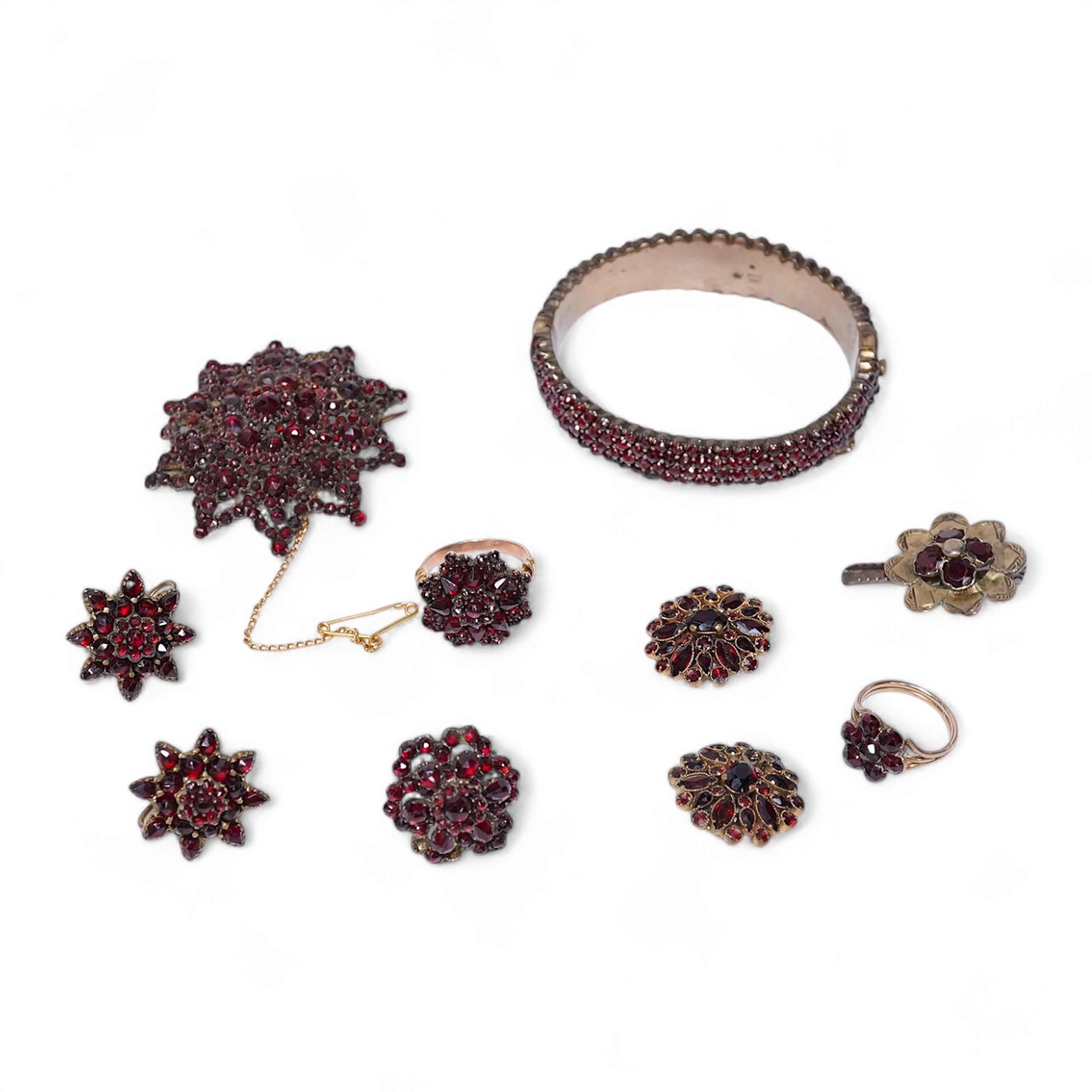 A suite of garnet and paste jewellery, comprising: a brooch, 5cm diameter; a bangle, inner circumference 16cm; two rings, sizes I and M; a pair of earrings, and a single earring, each set with rose-cut garnets; and a pai